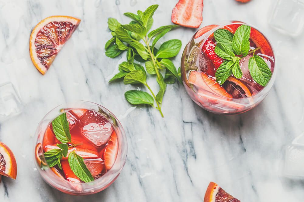 Blood orange and strawberry summer Sangria. Fruit refreshing rose wine cocktails in glasses with ice and mint over grey marble background, top view, square crop