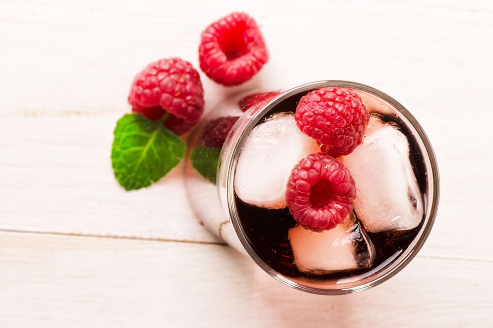Red raspberry drink with ice cube on a wooden background, view from above